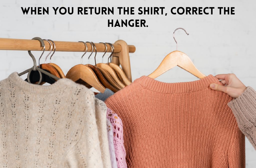 a woman holding a peach colored sweater on a wooden hanger that is backward