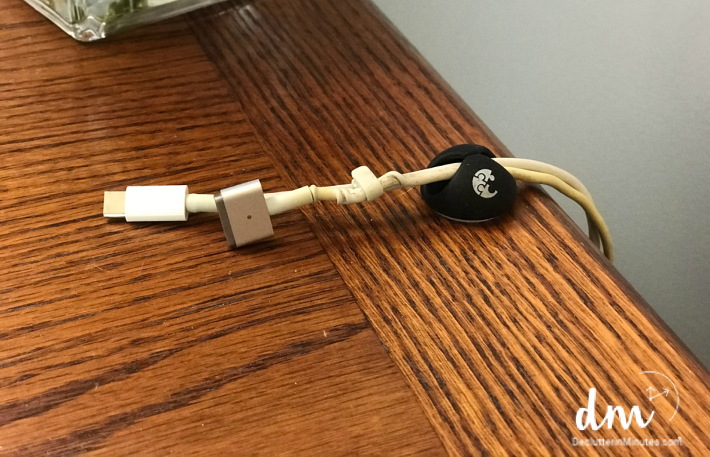 an adhesive cord holder on the end of a wood top desk holding 2 cords