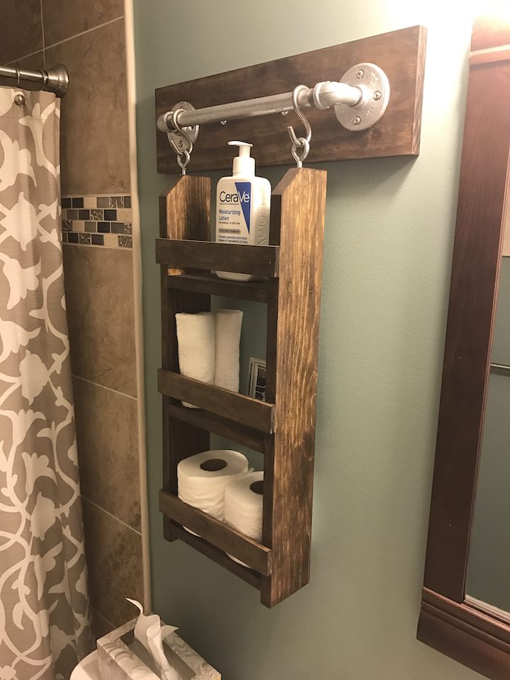 Image that shows a DIY wood shelf hanging on the bathroom wall that holds lotion, towels, and toilet paper. 