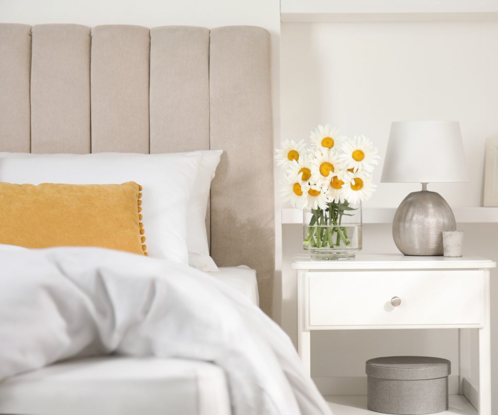Bouquet of beautiful daisy flowers and lamp on nightstand next to a bed