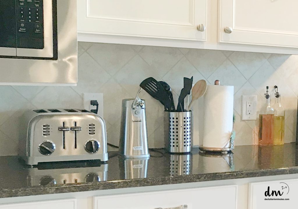 A kitchen countertop with a stainless steel toaster, utensil holder, paper towel roll, and bottles of cooking oil