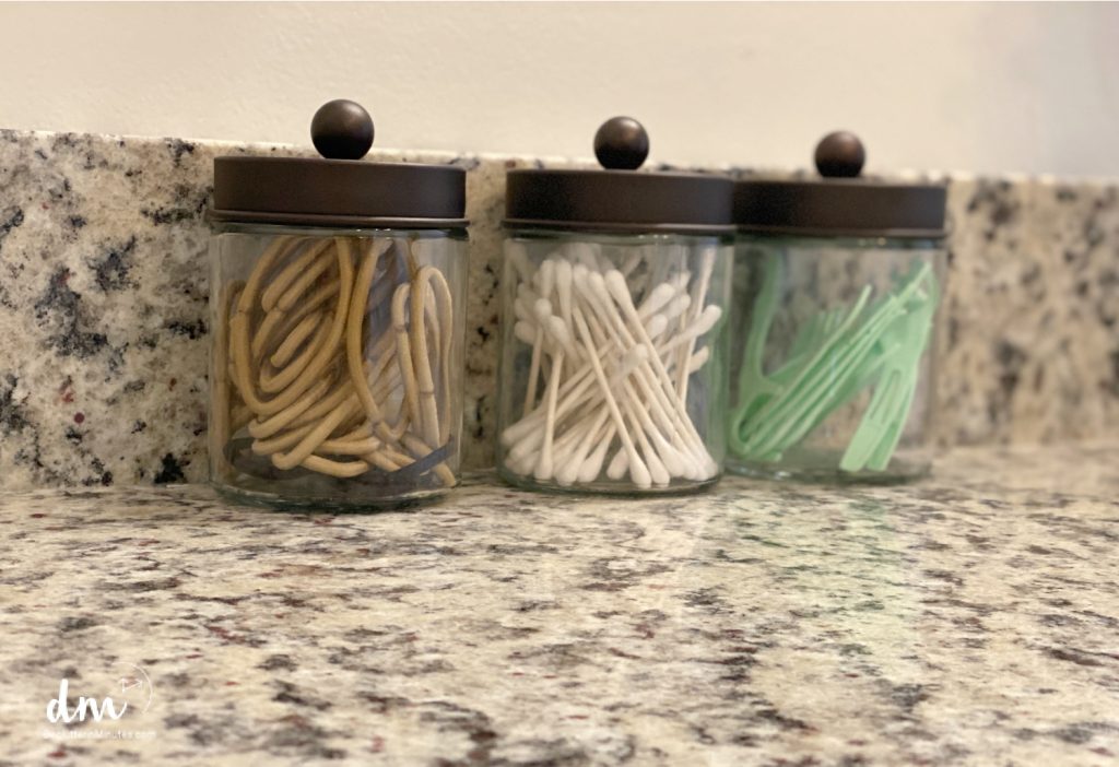 a counter top organized area of glass jars filled with bands, q-tips, and floss