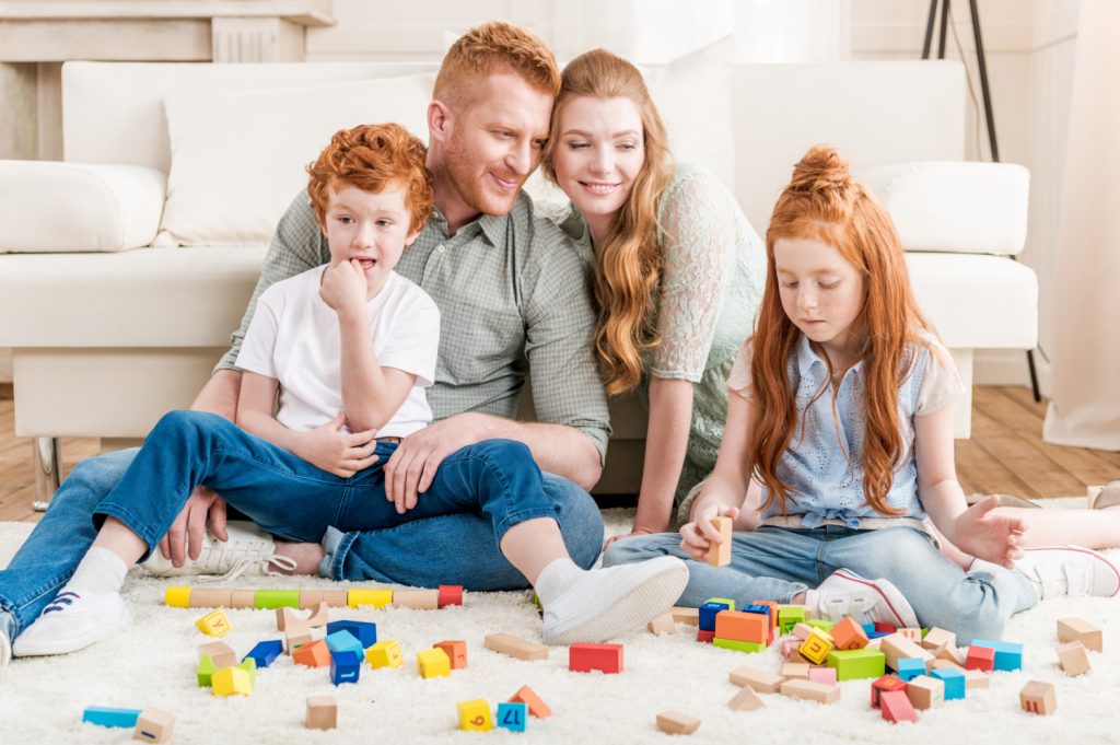 Family sitting on a carpet playing with colorful wooden blocks in a bright living room