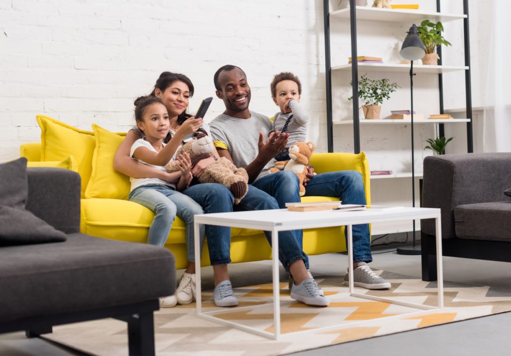 Smiling family sitting on a yellow sofa, enjoying time together with stuffed toys