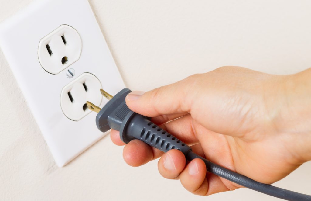 a hand unplugging a grey chord from an outlet
