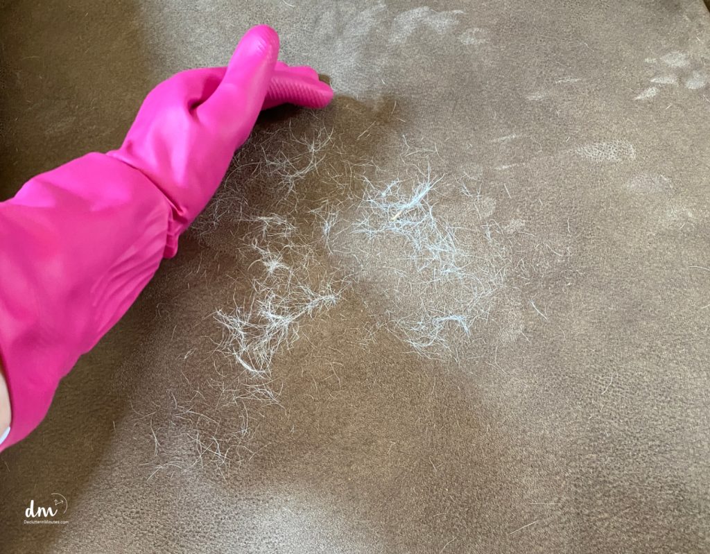a hand with a pink glove wiping dog hair into a pile on a cushion