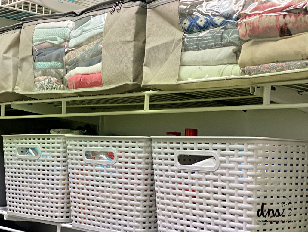 zipper bags filled with clothes on a closet shelf above a shelf with 3 grey baskets