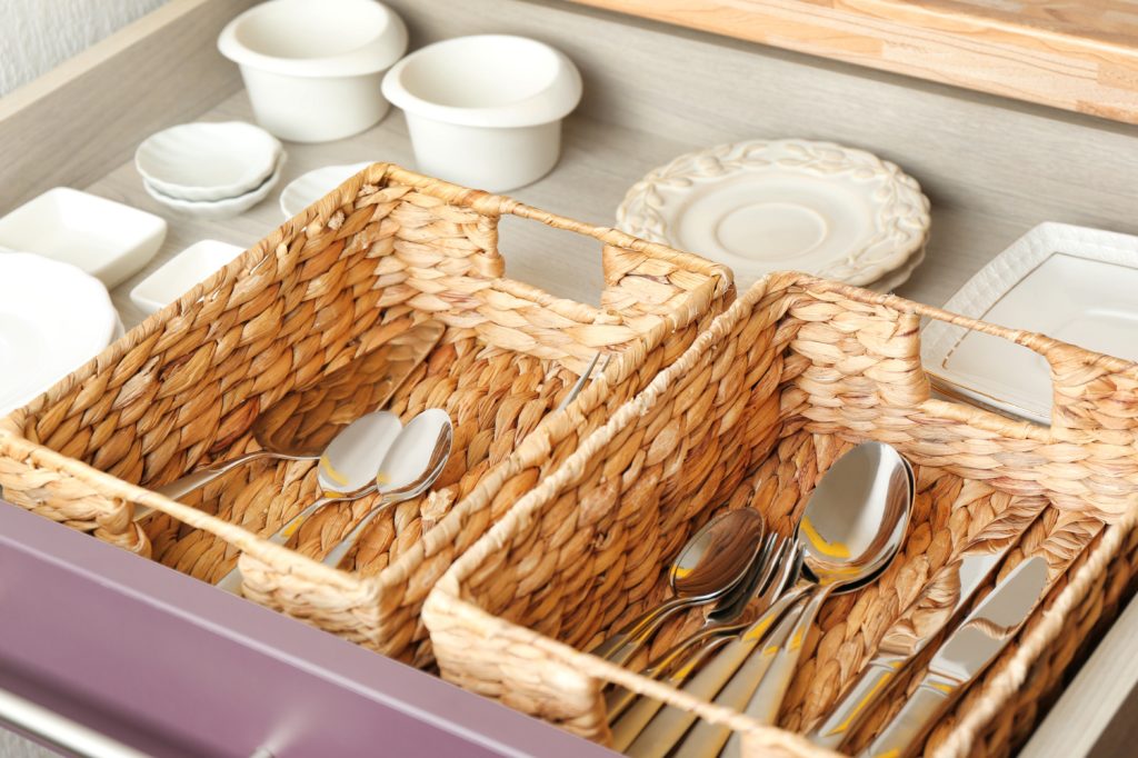 a kitchen drawer with silverware in whicker baskets