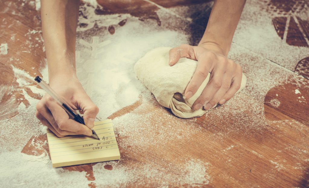 hand making notes on a note pad while needing bread with the other hand