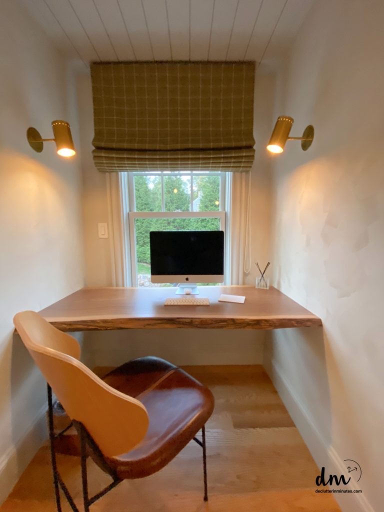 a desk with a computer on top with a brown chair in front of a window