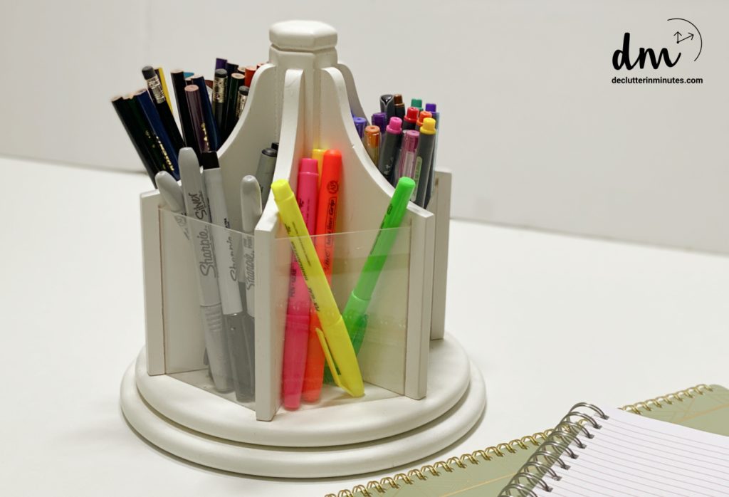 A wooded carousel organizer with pens, pencils and markers inside with 2 spiral notebooks in the lower corner