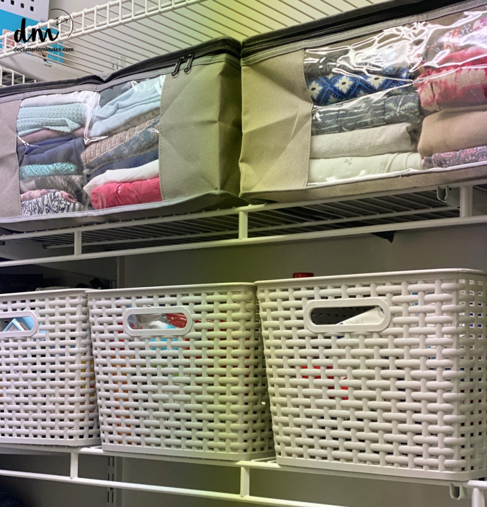 A closet with 3 grey baskets on the lower shelf and 2 zipper bags filled with folded clothes on the other shelf.