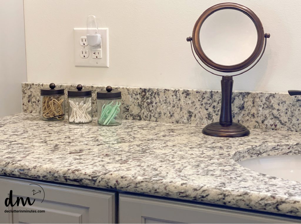 3 apothecary jars on next to a mirror on a countertop