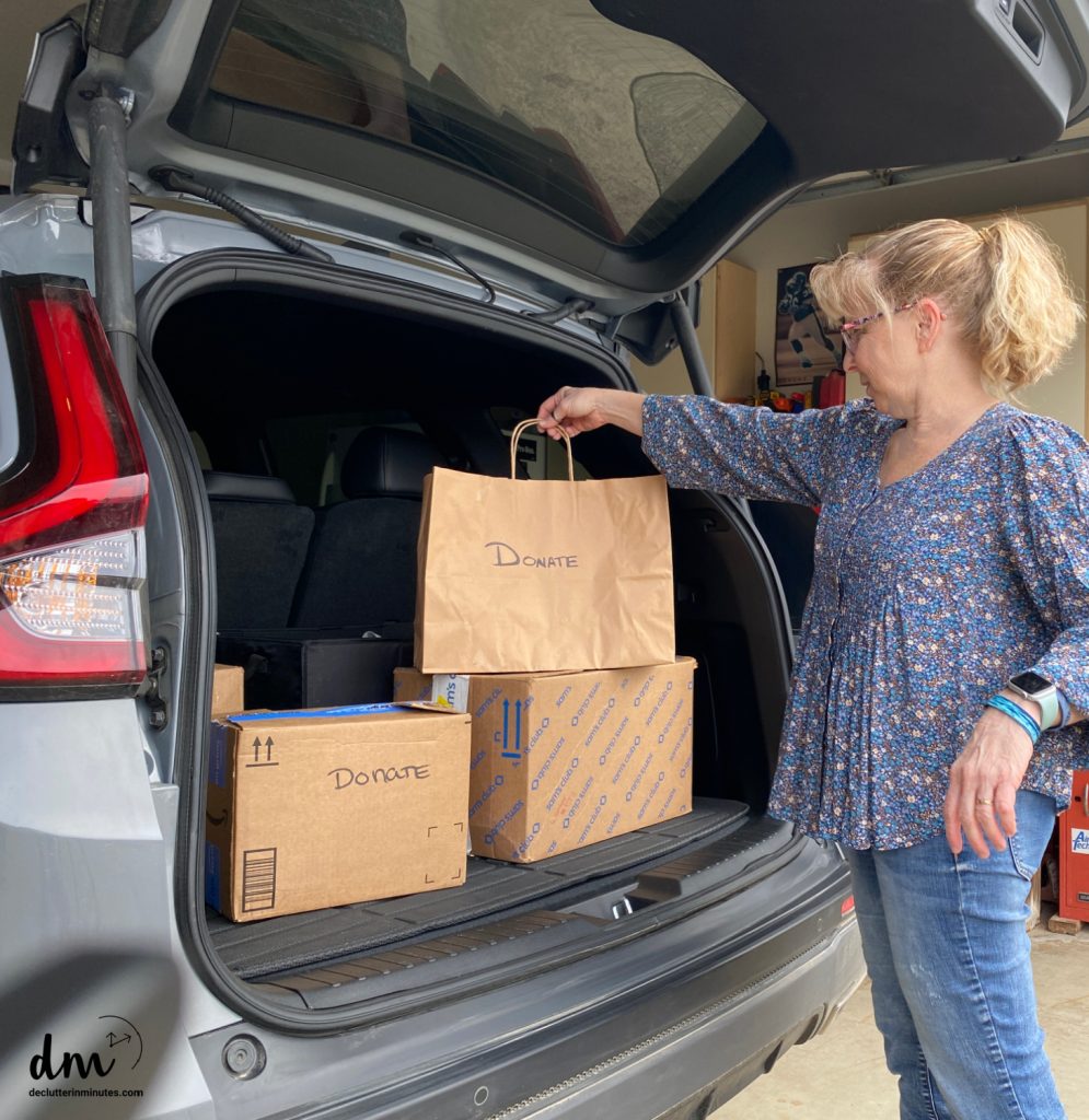 a woman in a blue shirt putting a donation bag into the back of her car