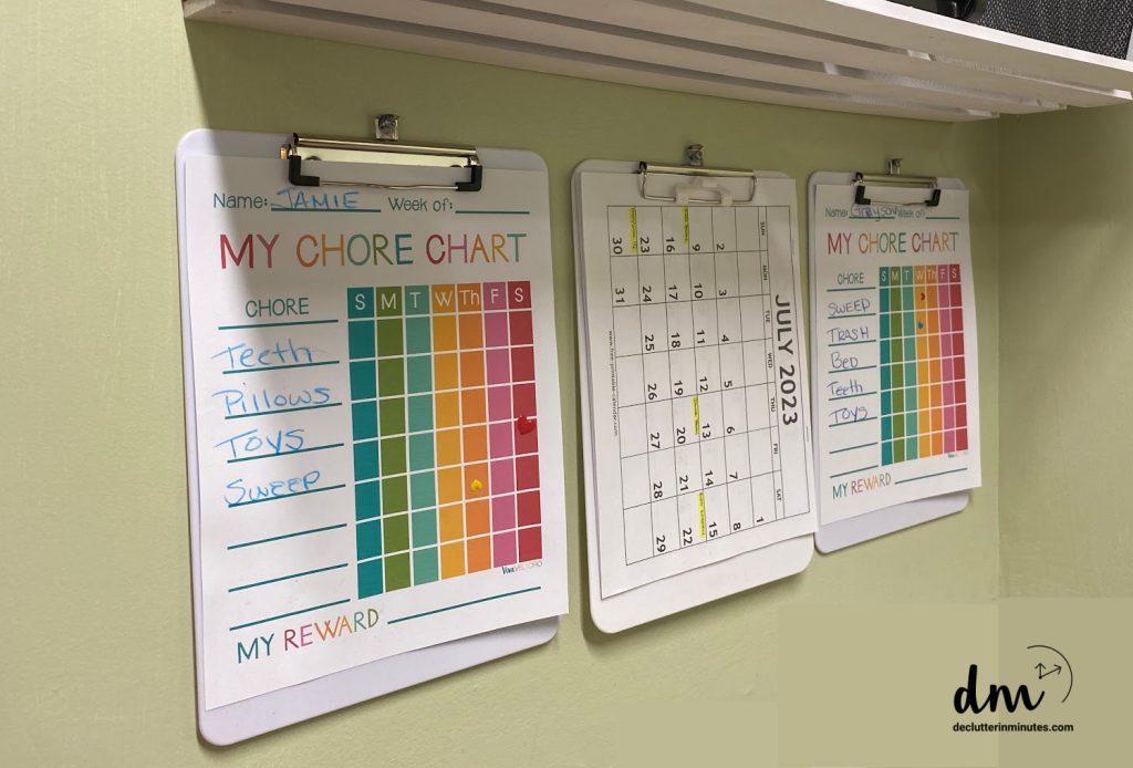 3 clipboards holding chore charts and a calendar hanging in a home hub set up