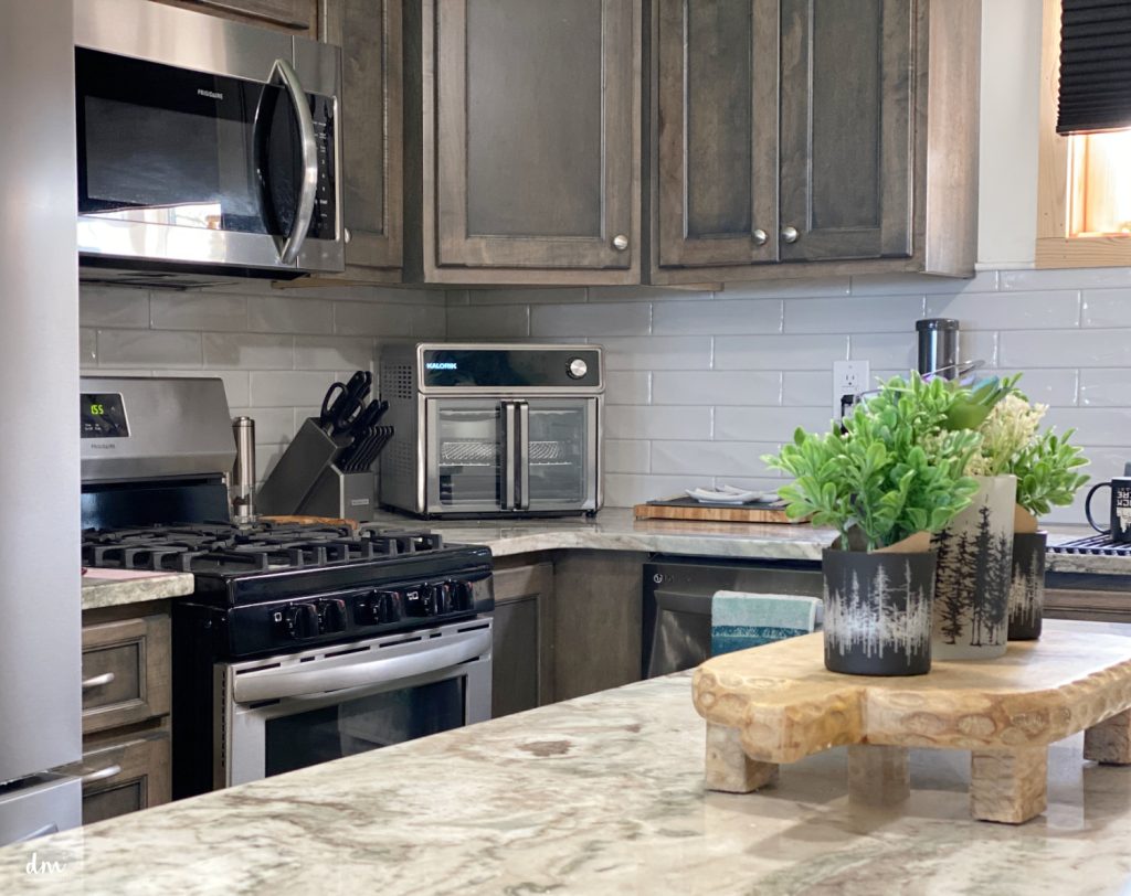 A modern kitchen with stainless steel appliances, a toaster oven on the counter, and a decorative plant arrangement on a wooden riser
