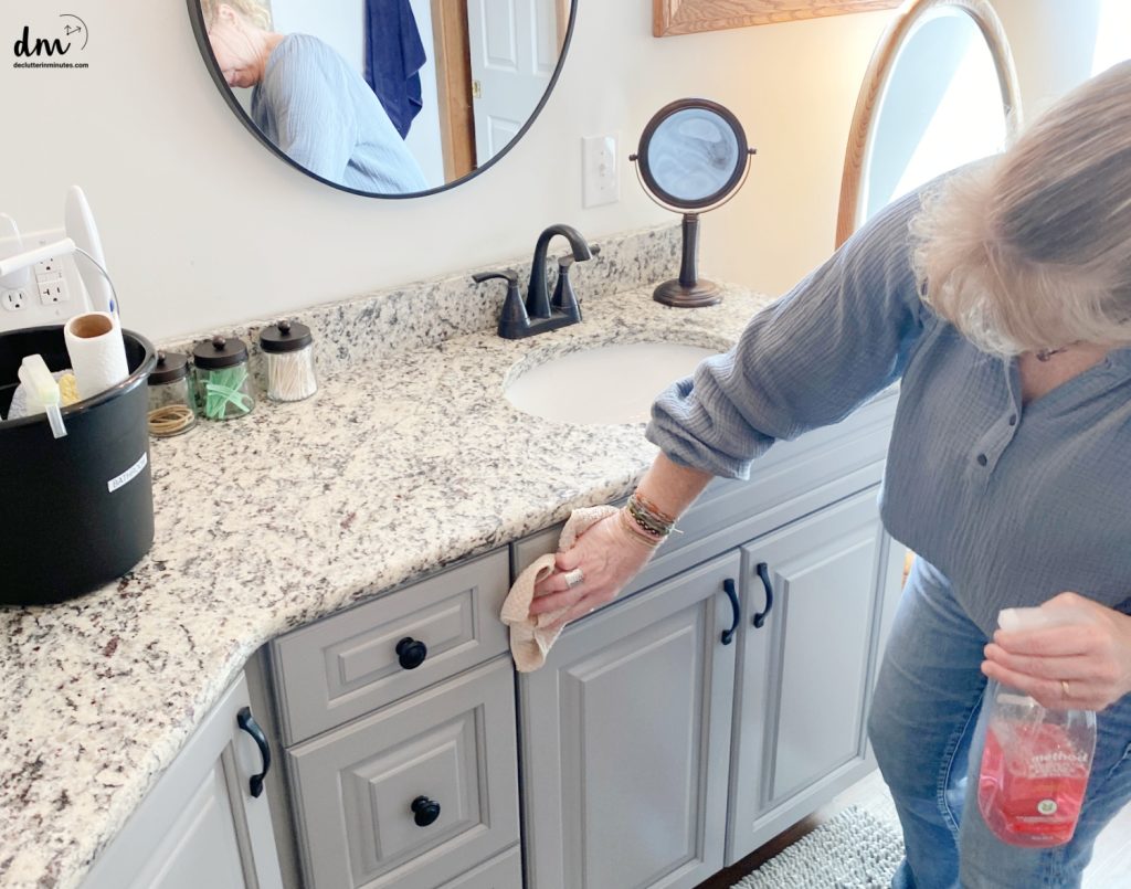 a woman wiping the front of the cabinets in a bathroom
