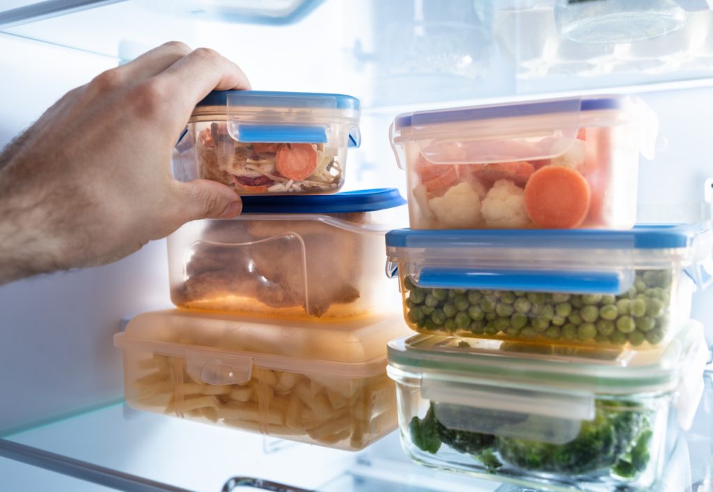 a hand reaching for a container of leftovers in a stack inside of a fridge