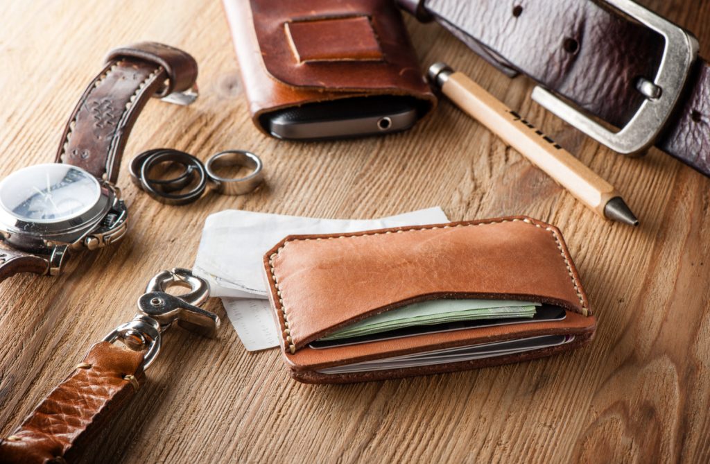 a cluttered dresser top covered with a wallet, keys, money, rings, belt
