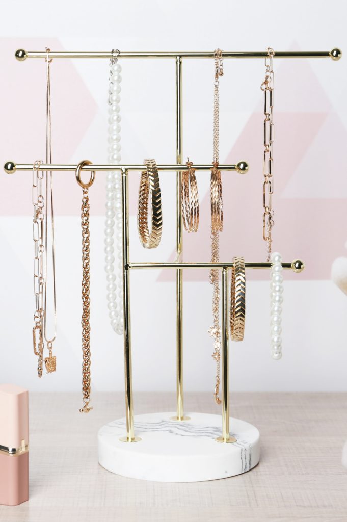jewelry hanging on a stand organizer in front of a pink wall