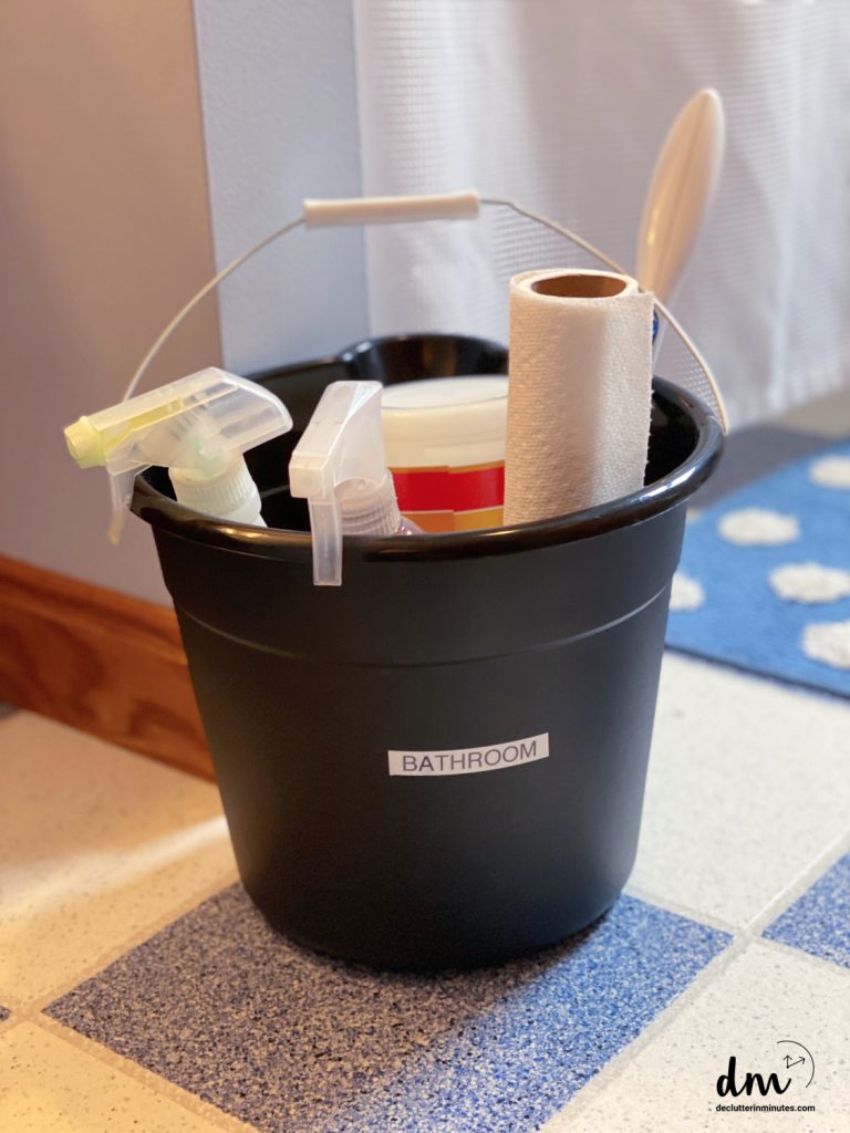 a black bucket labeled BATHROOM filled with cleaning supplies