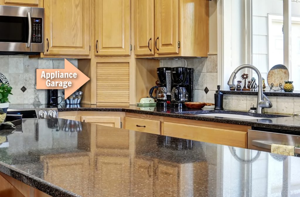 A spacious kitchen with light wood cabinets, with an arrow labeled "Appliance Garage" points to a roll-up cabinet door designed for storing small kitchen appliances
