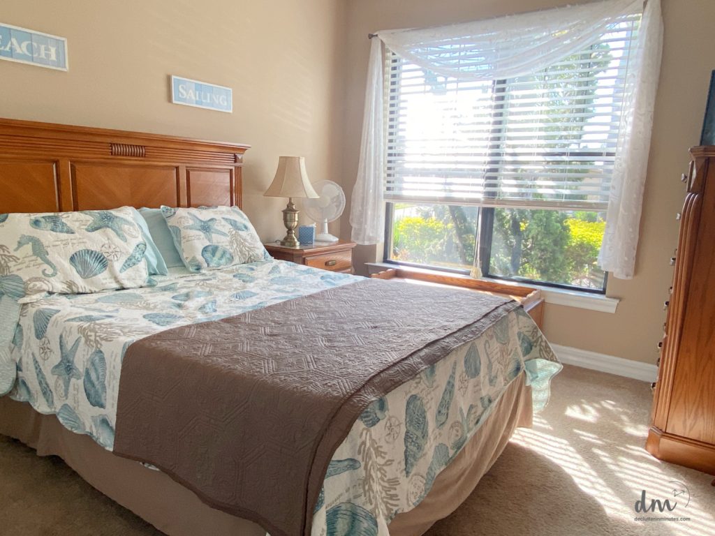 a white and blue bed with a brown blanket near to a large window