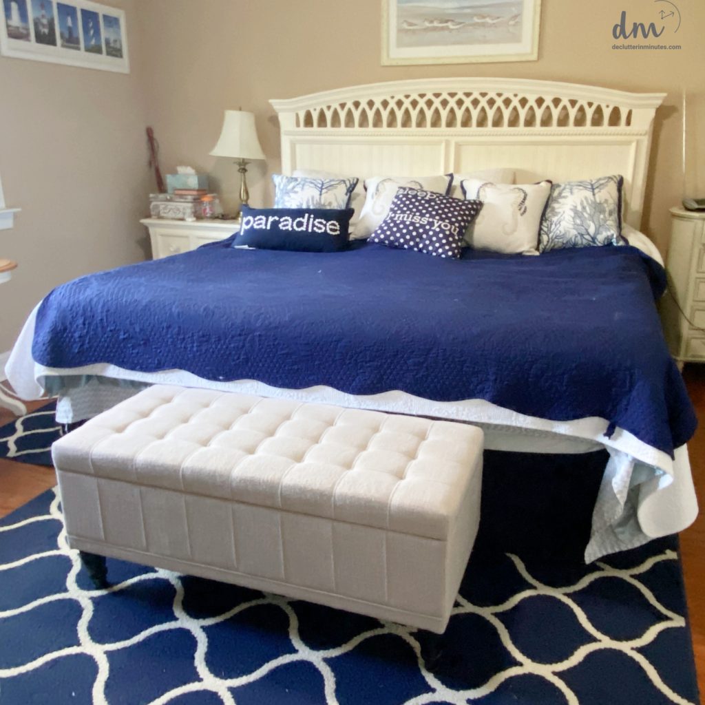 a white bed with a blue comforter and a shite ottoman at the foot