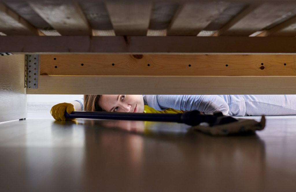 a woman using a vacuum to clean under a bed
