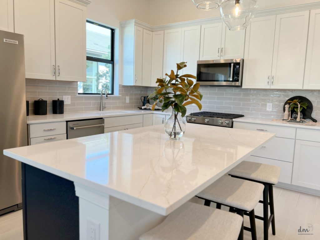 A modern kitchen with white cabinets, stainless steel appliances, a large marble island with bar stools, and a vase as a centerpiece