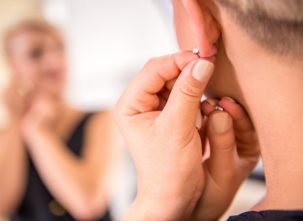 a woman putting on earrings looking into a mirror