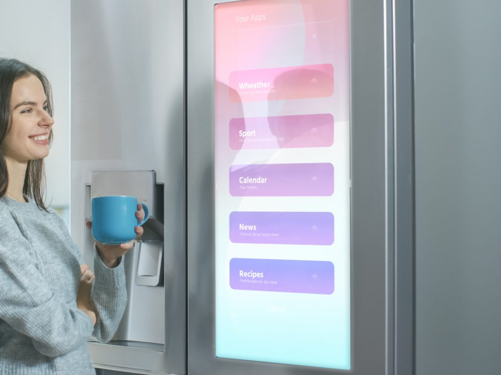 a couple looking at a computer screen on the front of a fridge