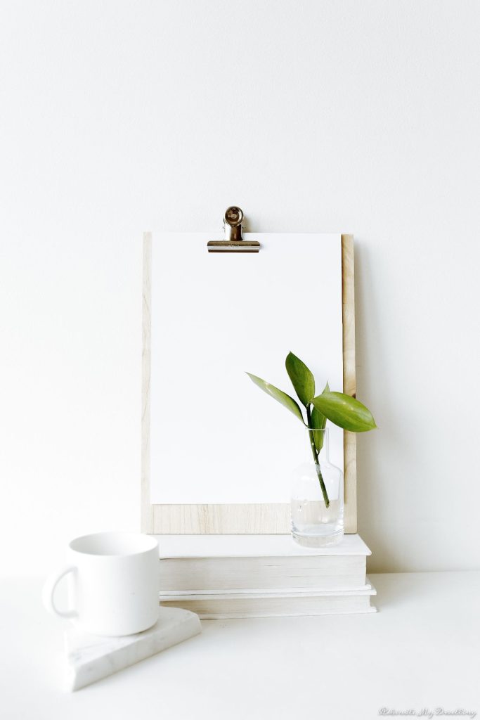 a clipboard with white white paper, white mug and plant decor