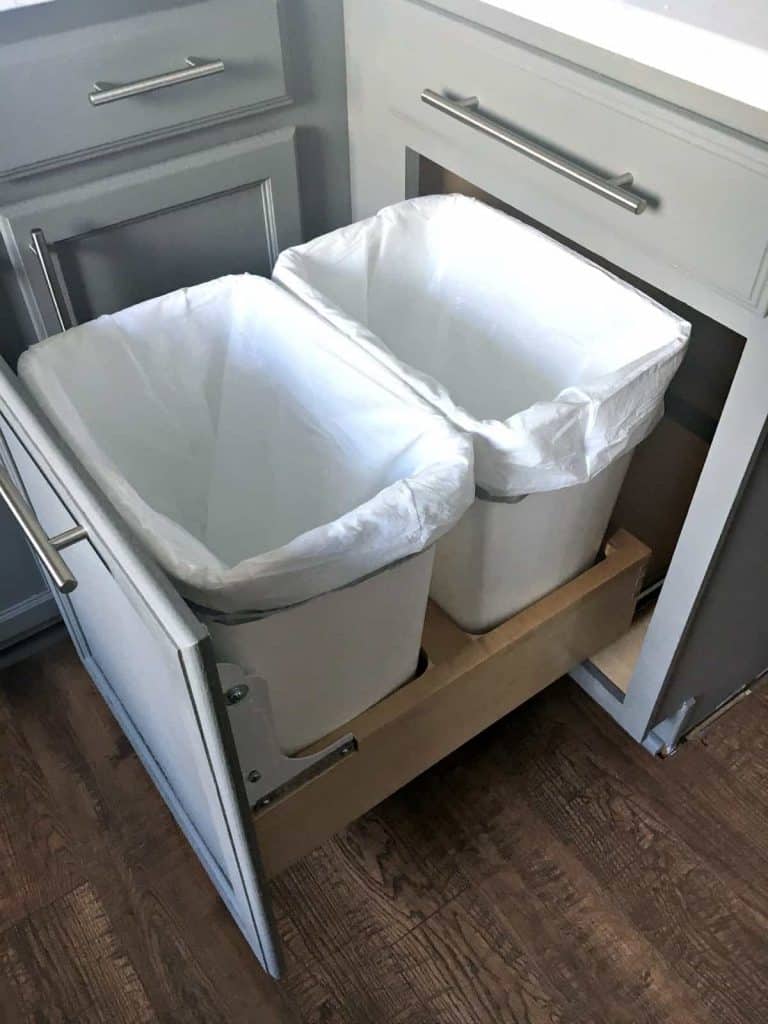 A pull-out cabinet drawer with two trash bins lined with white bags