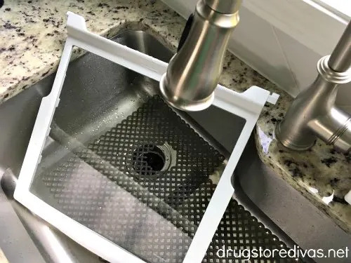 a disassembled refrigerator shelf being cleaned in a stainless steel kitchen sink