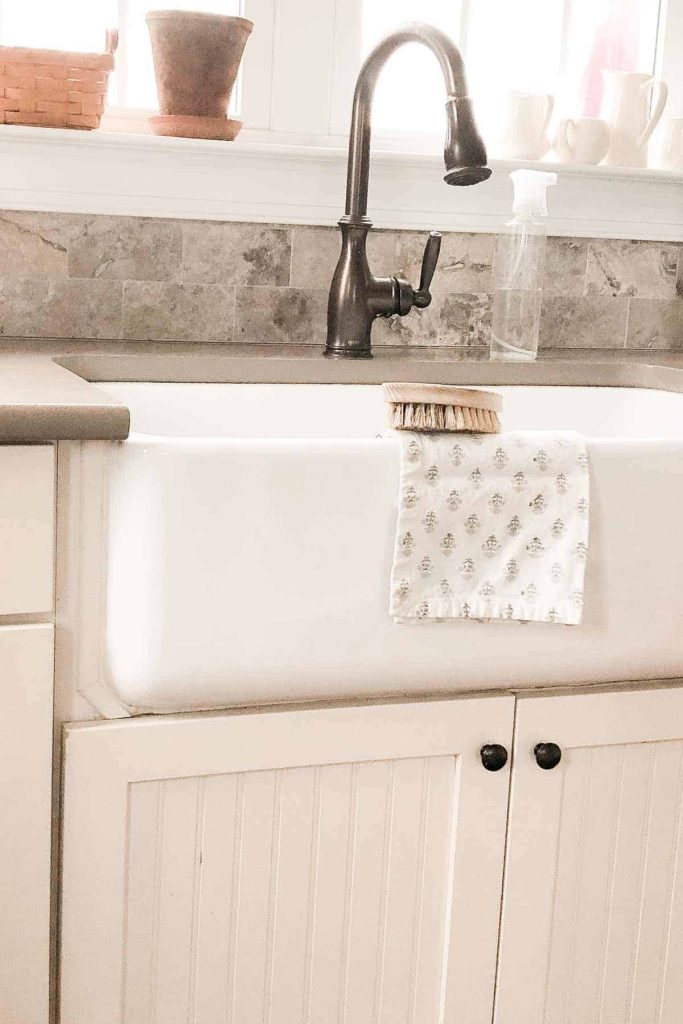A farmhouse sink, with a cleaning brush and a patterned towel