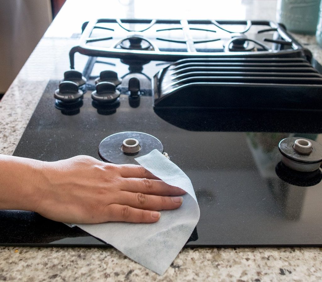 hand wiping a ceramic stove top with a white cloth