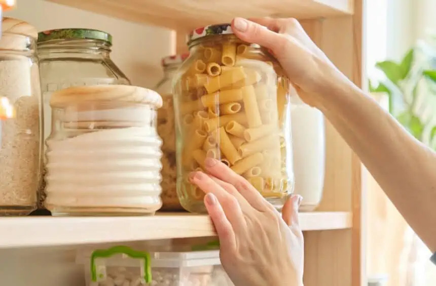 hands organizing glass jars filled with various dry food items, including pasta and grains