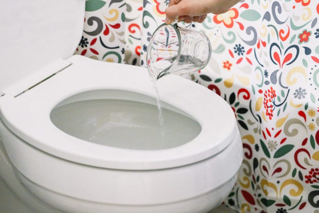 A person pours water from a measuring cup into a toilet
