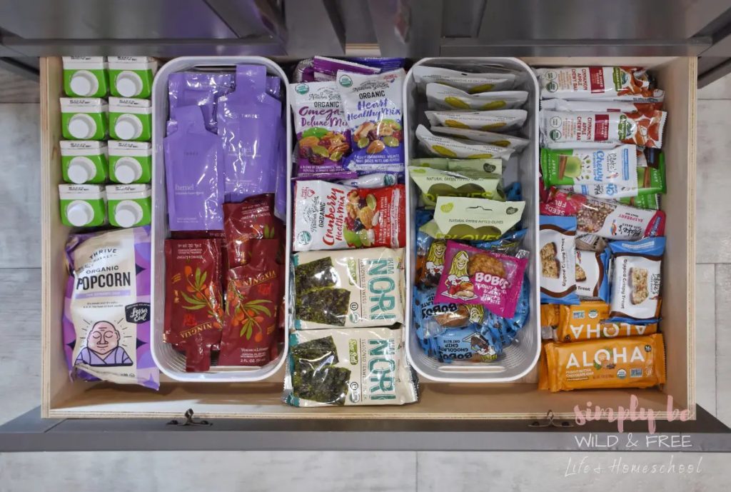 kitchen drawer organized with various pre-packaged snacks including popcorn, dried fruit, and granola bars
