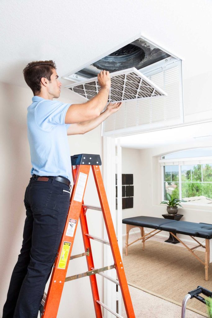 man on an orange ladder removing a vent cover from the ceiling