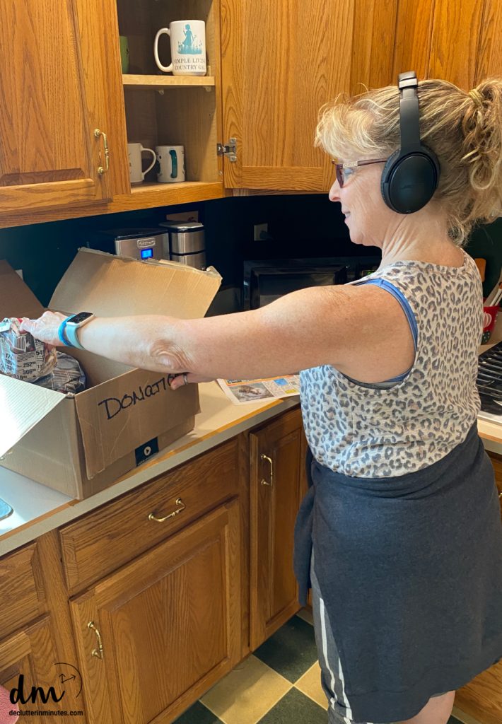woman with headphones on decluttering a kitchen cabinet