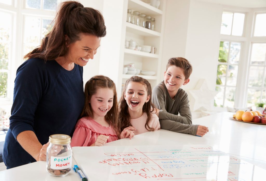 young mother with her three kids looking at a chore chart on a table
