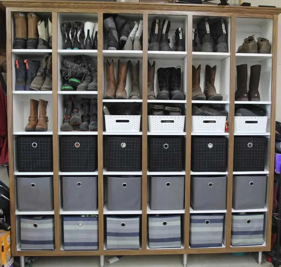 large wooden storage unit filled with boots and other shoes in open cubbies, along with several fabric bins for additional storage