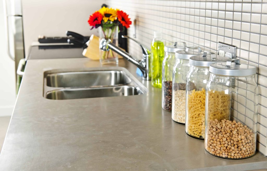 A clean kitchen countertop with a double sink, jars of dry goods, a knife block, and a vase of colorful flowers