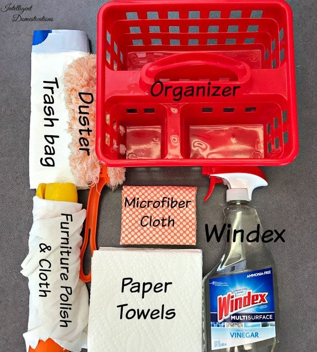 A red cleaning caddy with labeled items-a duster, microfiber cloth, Windex, paper towels, furniture polish and cloth, and a trash bag