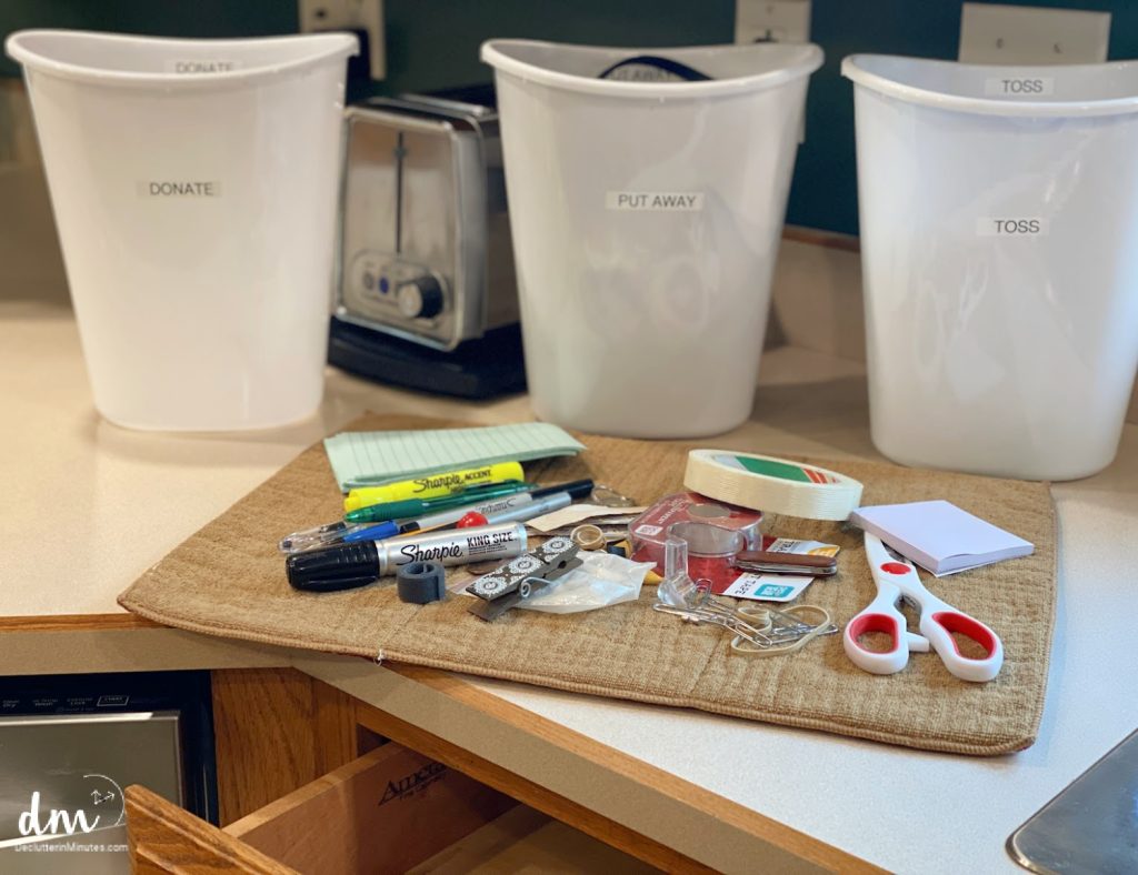 a towel on a counter with clutter on it and 3 white cans nest to an empty kitchen drawer