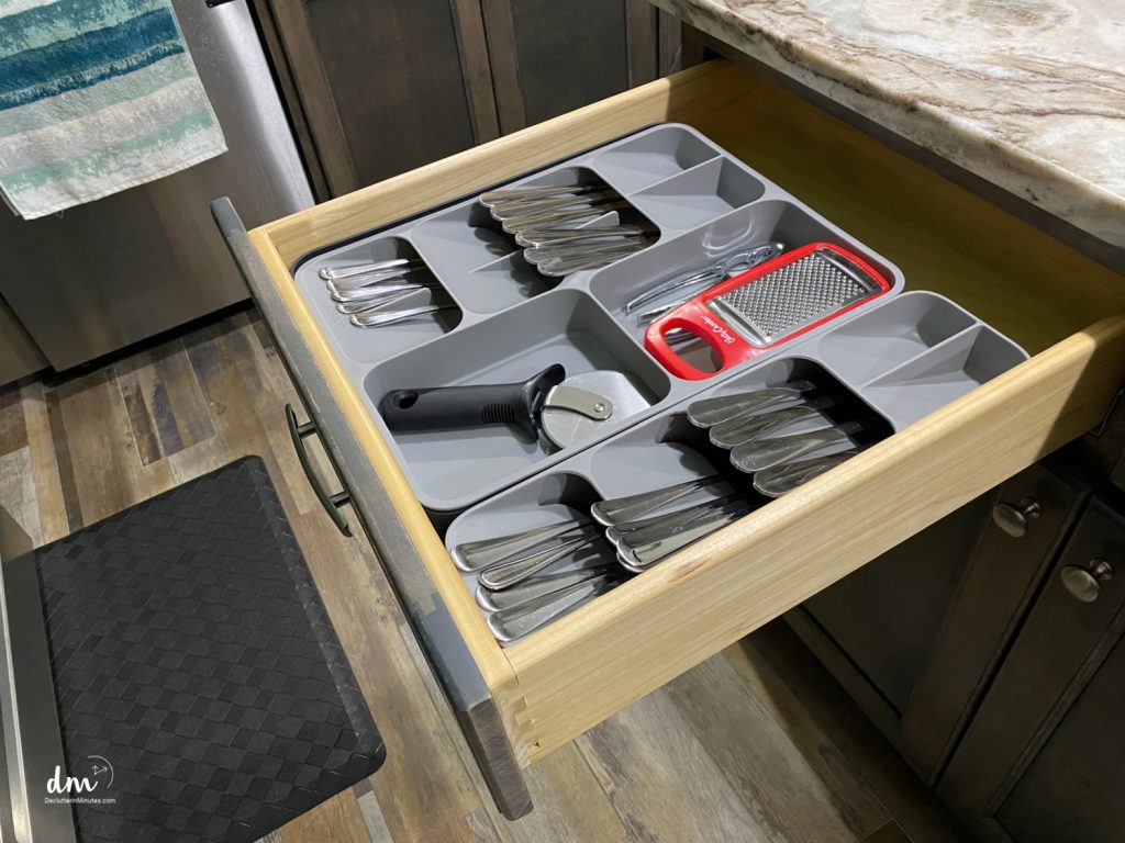 a kitchen drawer with silverware, a pizza cutter, and a grater neatly arranged in a gray plastic utensil tray
