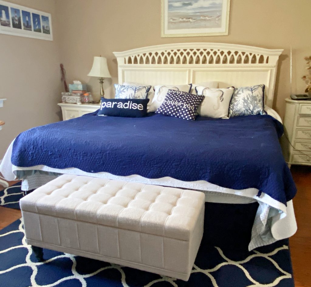 a white ottoman at the foot of a blue bed in a bedroom