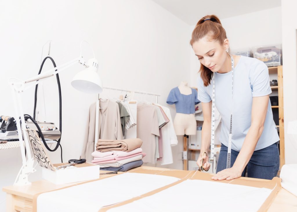 a woman cutting a pattern on a table in a sewing room